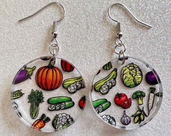 May include: A pair of round, clear acrylic earrings with a colorful vegetable print. The earrings feature a variety of vegetables, including pumpkins, cucumbers, eggplant, broccoli, and garlic.