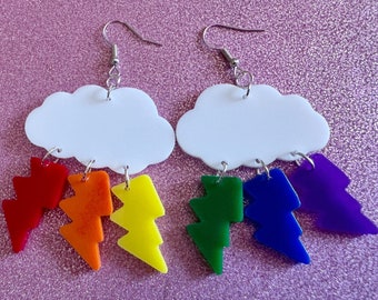 May include: A pair of rainbow lightning bolt earrings with a white cloud charm. The earrings are made of acrylic and have silver hooks.
