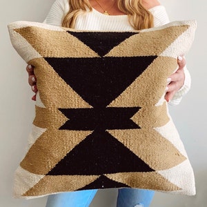 May include: A decorative pillow with a geometric design. The pillow features a pattern of black, tan, and cream-colored triangles. The pillow is rectangular and appears to be made of woven fabric.