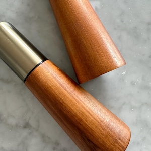 May include: Two wooden salt and pepper shakers with silver tops. The shakers are made of a light brown wood with a smooth finish.