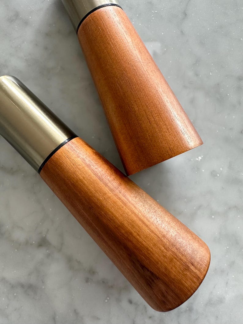 May include: Two wooden salt and pepper shakers with silver tops. The shakers are made of a light brown wood with a smooth finish.
