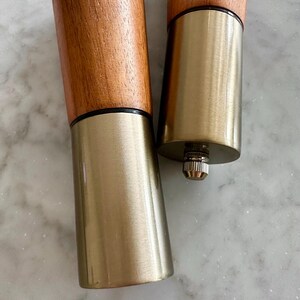 May include: Two wooden furniture legs with a gold metal base. The legs are brown and have a dark brown band around the top of the wood.
