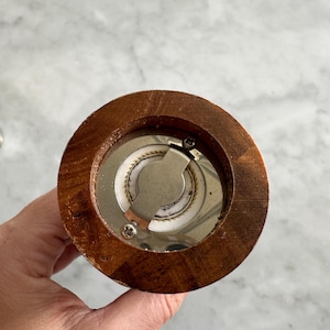 May include: Close-up of the bottom of a wooden pepper mill. The mill has a metal grinding mechanism with a screw.
