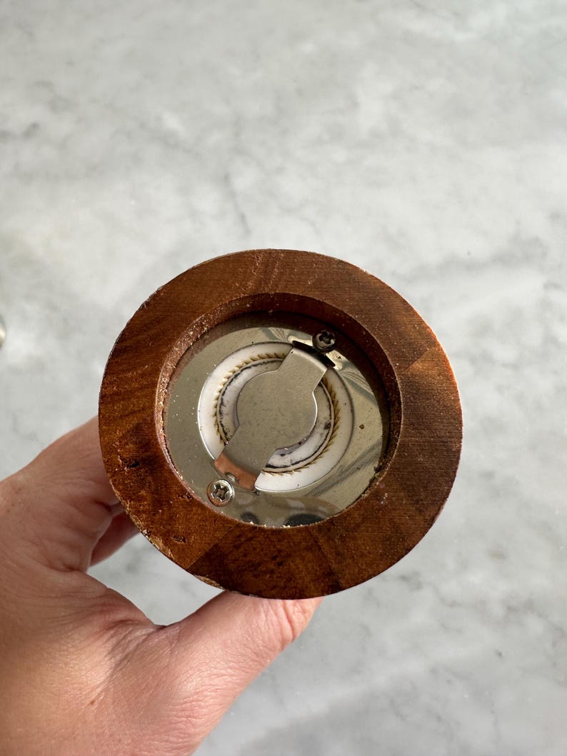 May include: Close-up of the bottom of a wooden pepper mill. The mill has a metal grinding mechanism with a screw.