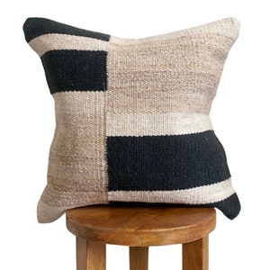 May include: A square throw pillow with a black and white geometric pattern. The pillow is made of a woven fabric and has a beige background.