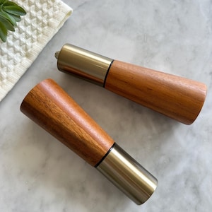 May include: Two wooden salt and pepper shakers with a silver metal top. The shakers are on a white marble surface.