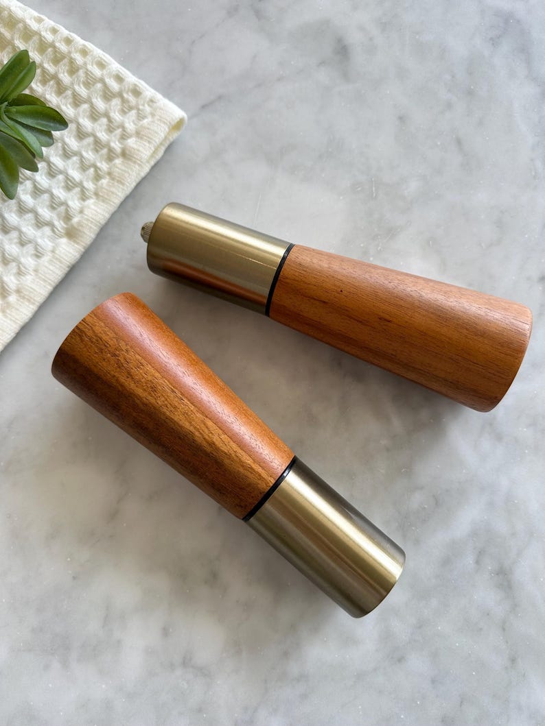 May include: Two wooden salt and pepper shakers with a silver metal top. The shakers are on a white marble surface.