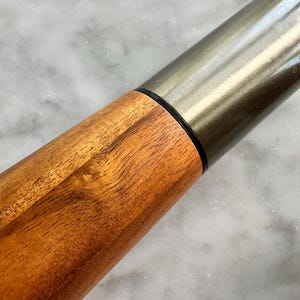 May include: A wooden rolling pin with a silver metal top. The wood has a natural brown color and a smooth finish.