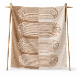 May include: A beige and brown patterned throw blanket displayed on a wooden rack. The blanket features a repeating design of curved lines, with a colour block design. The left side is brown, and the right side is beige.