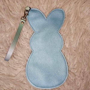 May include: A light blue bunny-shaped pouch with a light green and silver strap. The pouch is made of a textured material and has a small loop at the top for attaching a key ring.