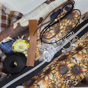 May include: A craft kit containing a sunflower-patterned fabric panel, a black zipper with silver hardware, a roll of black webbing, a brown faux leather strip, a thin dark brown cord, metal swivel clips, and a small round sticker with a daisy.