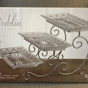 May include: A Dublin Crystal three-tiered rectangle server featuring three clear, rectangular glass trays with a diamond-cut pattern, supported by a silver-toned metal stand with curved, scroll-like legs and arms.