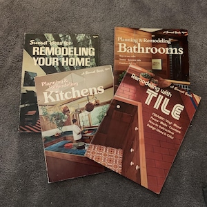 May include: A selection of vintage Sunset Books on home renovation. Titles include "Remodeling Your Home," "Planning & Remodeling Bathrooms," "Planning & Remodeling Kitchens," and "Remodeling with Tile." The books have colourful covers with design ideas.