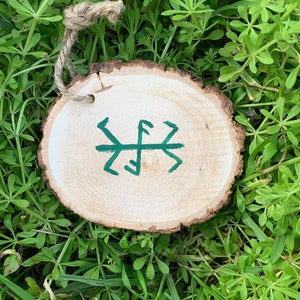 May include: A wooden round ornament with a green painted symbol on it. The ornament is hanging from a twine string.