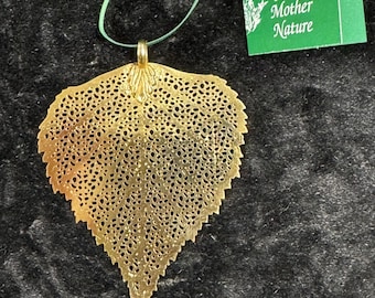 May include: A gold-colored leaf-shaped ornament with intricate cut-out details, suspended by a green ribbon. The ornament is paired with a green tag that reads "An Ornament From Mother Nature."