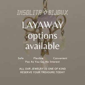 May include: A gold-toned pendant with a purple gemstone and pearl accents. The text "INSOLITA BIJOUX LAYAWAY options available" is displayed below the pendant. The text "Safe Flexible Convenient Pay As You Go, No Interest" is displayed below the pendant. The text "ALL OUR JEWELRY IS ONE OF KIND RESERVE YOUR TREASURE TODAY" is displayed below the text.