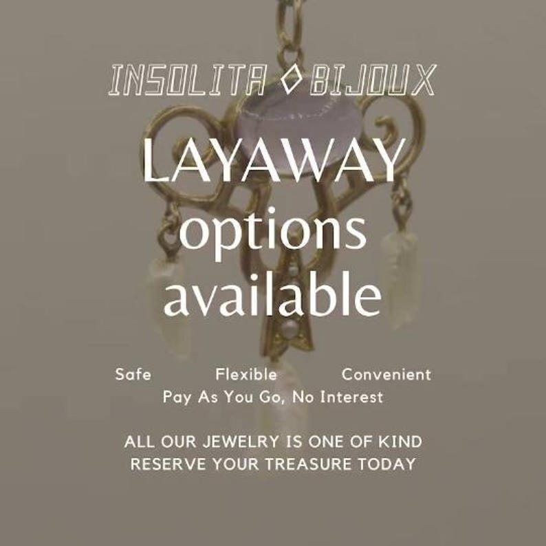 May include: A gold-toned pendant with a purple gemstone and pearl accents. The text "INSOLITA BIJOUX LAYAWAY options available" is displayed below the pendant. The text "Safe Flexible Convenient Pay As You Go, No Interest" is displayed below the pendant. The text "ALL OUR JEWELRY IS ONE OF KIND RESERVE YOUR TREASURE TODAY" is displayed below the text.