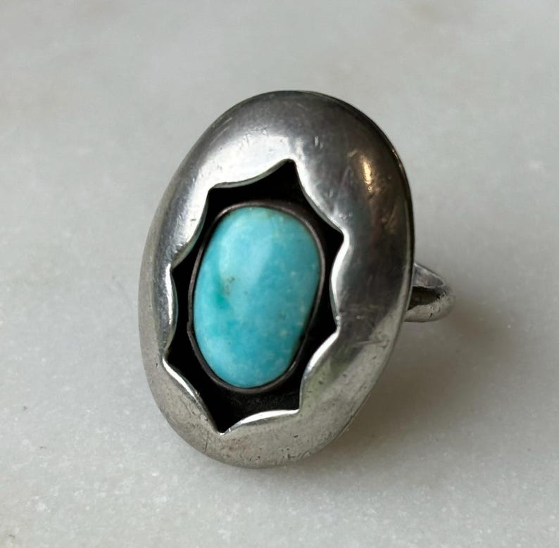 May include: A silver ring with a turquoise stone set in a starburst design.