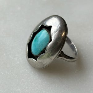 May include: A silver ring with a turquoise stone set in a starburst design.