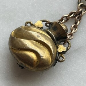 May include: A vintage gold-toned pendant necklace. The pendant is an oval shape with a textured, swirling design. It has decorative floral accents and is attached to a delicate chain. The metal has an aged appearance.