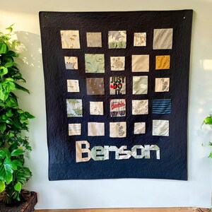 May include: A black quilt with a patchwork design. The quilt is made up of squares of different fabrics, including some with printed designs. The quilt is decorated with the name "Benson" in large letters and the phrase "Just Do It" in red and white letters.