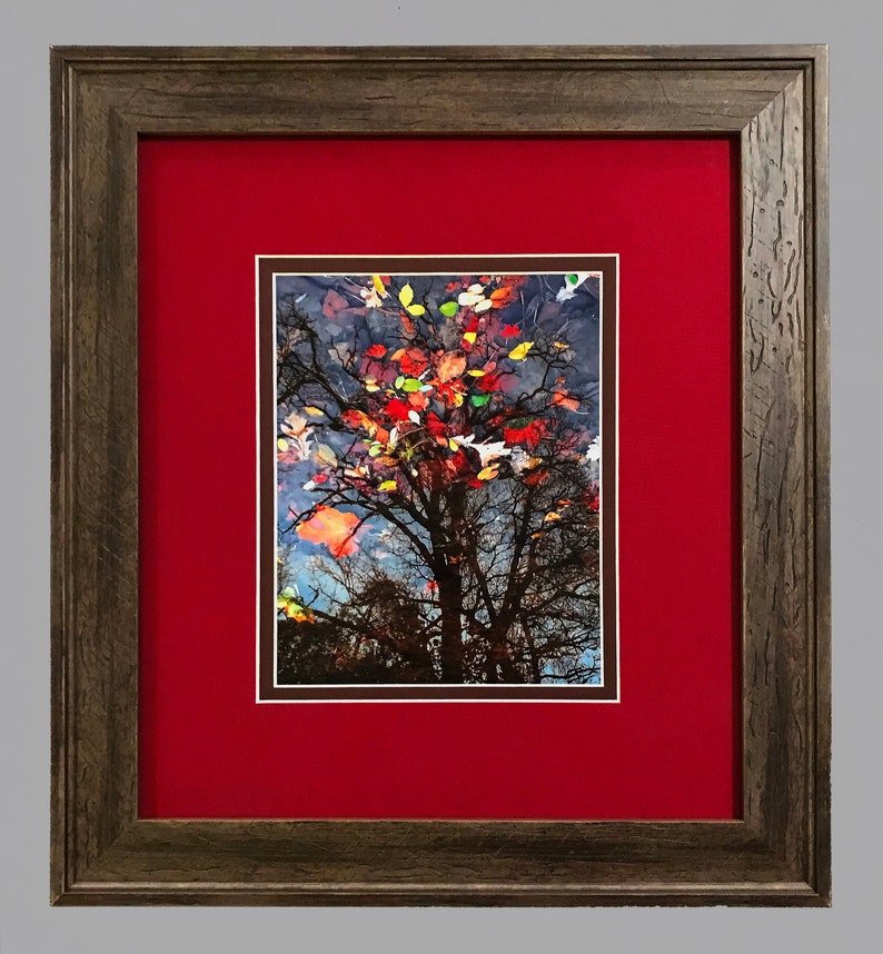 May include: Framed art print featuring a tree with colorful autumn leaves reflected in water. The artwork is set against a red mat and framed in a rustic, textured brown frame. The image captures the beauty of fall.