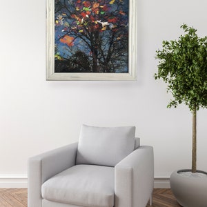 May include: A framed artwork featuring a tree with colorful leaves against a dark blue sky. The artwork is in a white distressed frame. The image is displayed above a gray armchair and next to a potted tree.