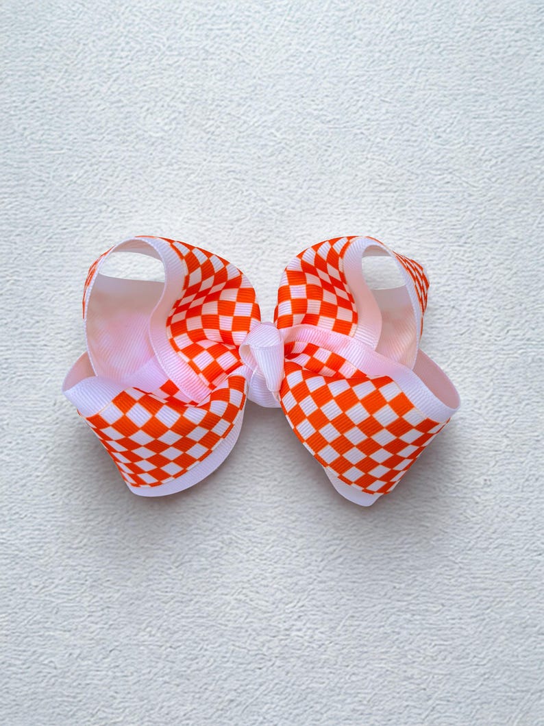 May include: A hair bow constructed from grosgrain ribbon featuring a vibrant orange and white checkered pattern. The bow is designed with multiple loops and a central knot, showcasing a structured, layered appearance with clean, crisp edges.
