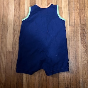 Puede incluir: Un pelele de beb&eacute; azul marino con cuello redondo y dise&ntilde;o sin mangas. El cuello y las sisas est&aacute;n ribeteados con un acento verde claro y naranja. El pelele est&aacute; hecho de una tela suave.