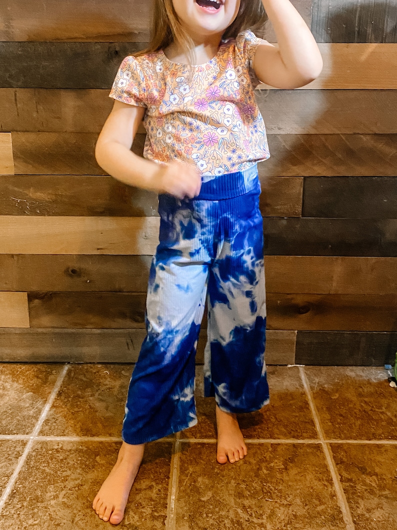May include: A young girl wearing a short-sleeved, floral print top and blue tie-dye pants.