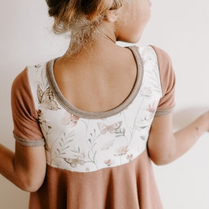 Pu&ograve; includere: Un vestito marrone e bianco con stampa floreale e bordatura marrone. Il vestito ha maniche corte e una scollatura rotonda.