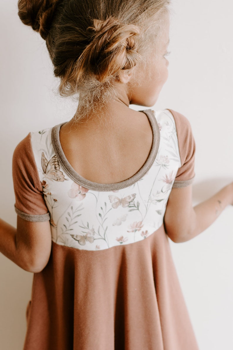 Pu&ograve; includere: Un vestito marrone e bianco con stampa floreale e bordatura marrone. Il vestito ha maniche corte e una scollatura rotonda.
