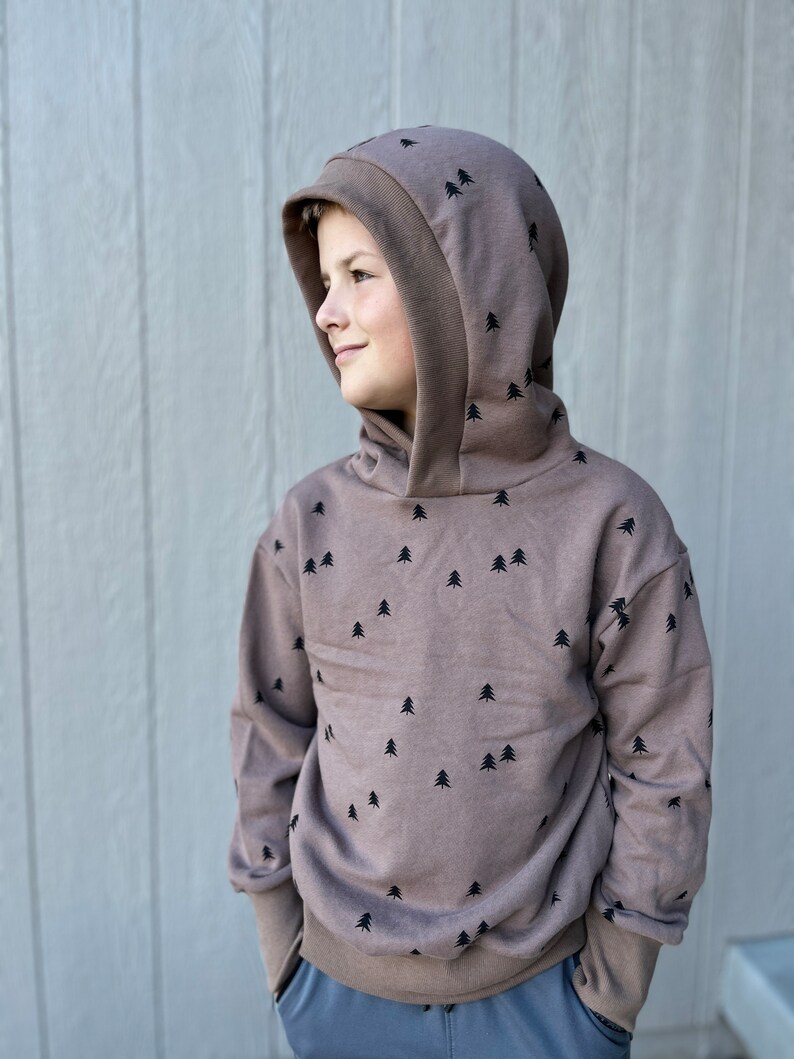 May include: A brown hooded sweatshirt with a black tree pattern. The sweatshirt has a double layer hood and a relaxed fit.