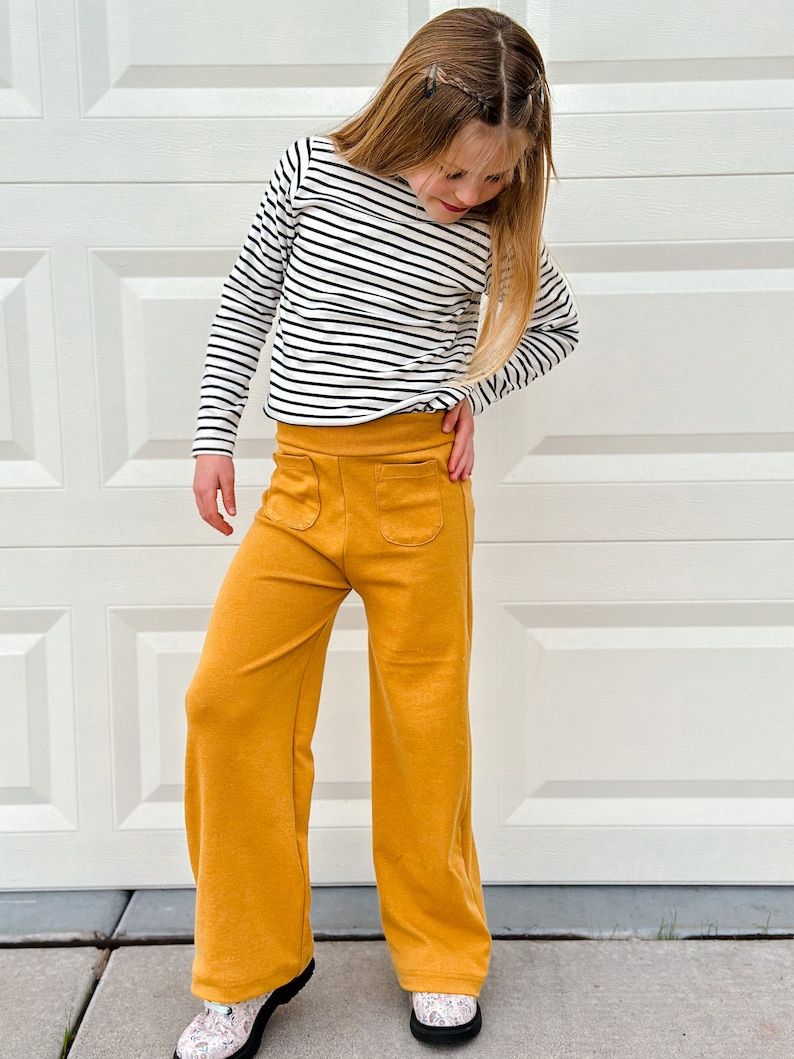 May include: A young person wearing a black and white striped long-sleeved shirt and mustard yellow wide-leg pants. The pants have two large pockets on the front.