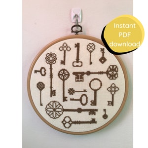 May include: A brown embroidery hoop with a white background and a pattern of brown keys. The hoop is hanging on a white wall with a white hook.