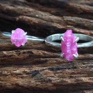 May include: Two silver rings with pink crystal gemstones. The rings are set on a wooden surface.