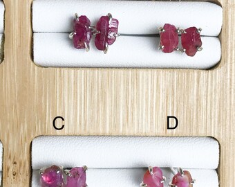 以下が含まれることがあります： 生のルビーの宝石が付いたイヤリングが4組。イヤリングは、白いフェルトの裏地が付いた木製のボードに展示されています。イヤリングには、A、B、C、Dのラベルが付いています。