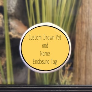 Op de afbeelding: Een gele ovale sticker met zwarte tekst die "Custom Drawn Pet and Name Enclosure Tag" luidt.