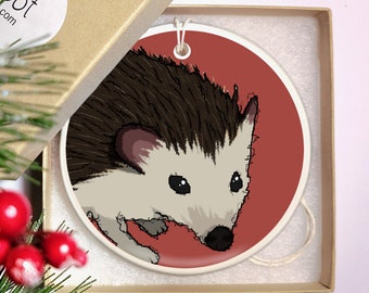 May include: A ceramic ornament featuring a cartoon illustration of a hedgehog with brown fur and a white face. The hedgehog is on a red background.