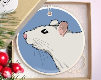 May include: A white ceramic ornament with a hand-drawn illustration of a white rat on a blue background. The ornament has a string for hanging.