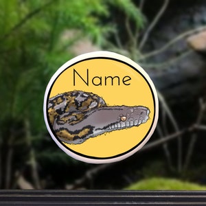 May include: A yellow circle sticker with a cartoon snake on it. The snake is gray and black with a yellow eye. The text "Name" is printed in black on the sticker.