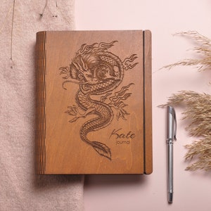May include: A wooden journal with a carved dragon design and the text "Kate journal" on the front.