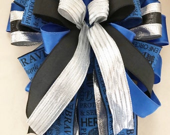 May include: A blue, black, and silver ribbon bow with the words "Protect & Serve", "Hero", "Brave", "Peace Makers", and "Enforcer" printed on the ribbons.