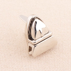 Könnte beinhalten: Ein glänzender silberfarbener Metallverschluss, wahrscheinlich für eine Tasche oder einen Geldbeutel. Der Verschluss hat eine rechteckige Basis mit gewölbter Oberseite und einem spitz zulaufenden, gewölbten Verschluss. Das Metall hat eine polierte, reflektierende Oberfläche.