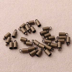 Könnte beinhalten: Eine Gruppe von 25 antiken goldfarbenen Metall-Endkappen für Kordeln oder Schmuckherstellung. Die Endkappen sind zylindrisch mit einer kleinen Schlaufe oben.