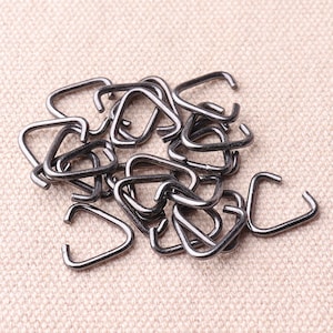 May include: A pile of silver-coloured metal jump rings. The rings are small and have a rounded shape.