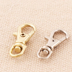 May include: Two metal clasps, one gold and one silver, on a beige fabric background.