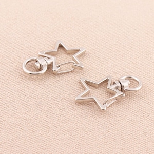 May include: Two silver star-shaped keyrings with a swivel clasp. The keyrings are made of metal and have a polished finish.
