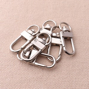 Puede incluir: Cinco cierres de metal plateado giratorios, también conocidos como broches de presión, para sujetar correas o cadenas a bolsos, carteras u otros accesorios.