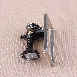 May include: A miniature black sewing machine with gold floral details and a silver base. The machine is in a tilted position, showing the top and side views.